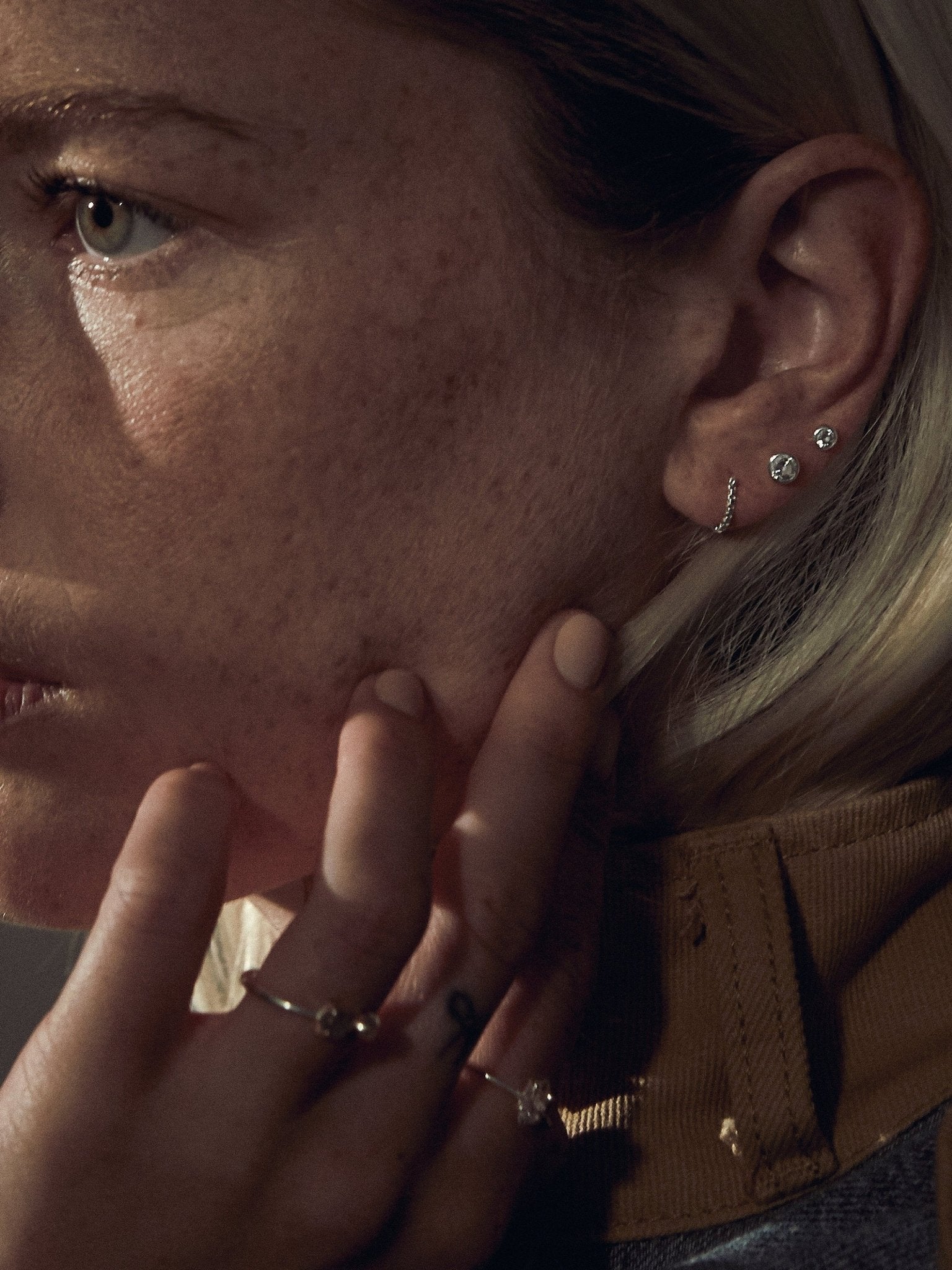 Emotional shot with gold earrings, model resting hand on face