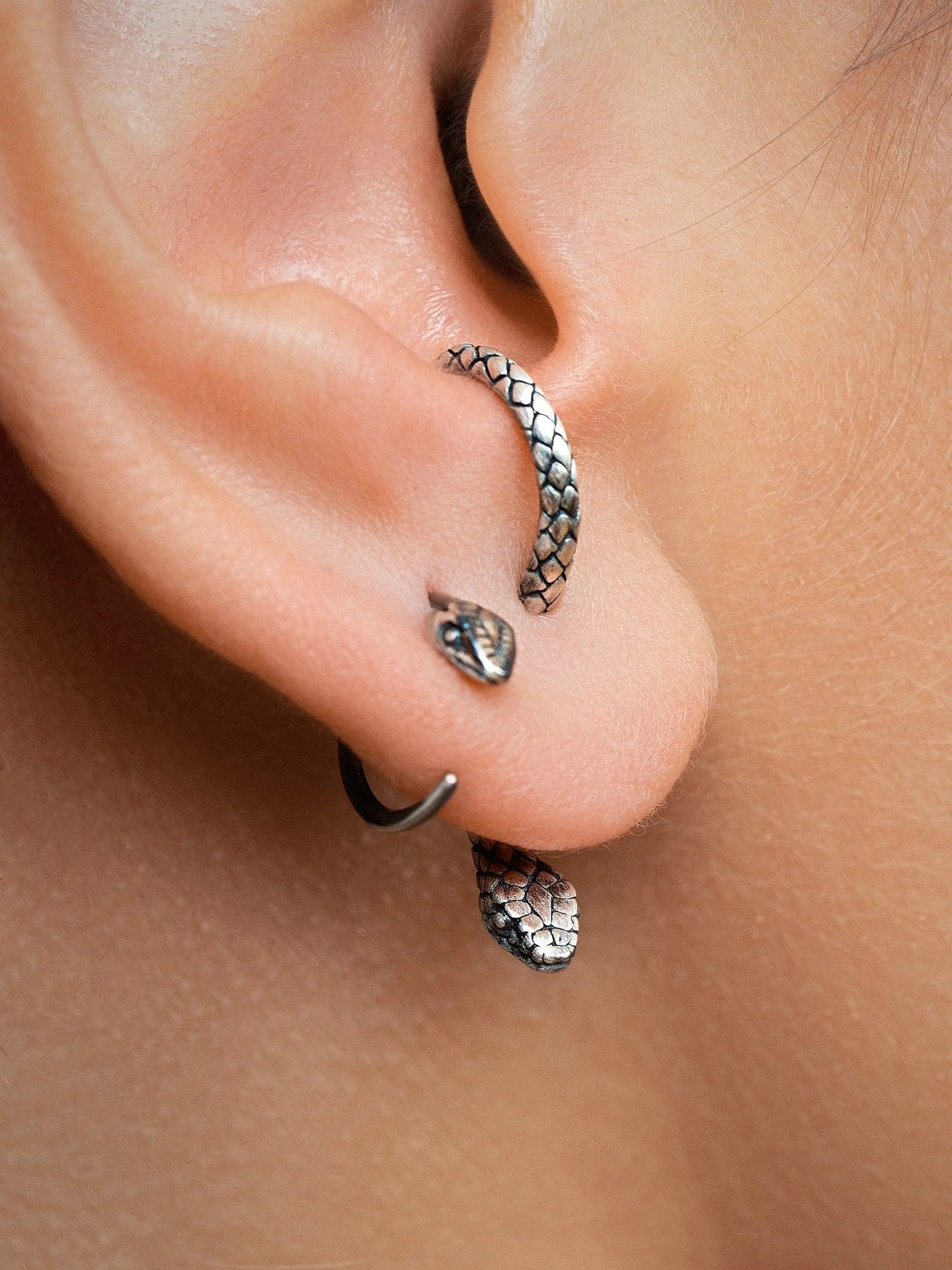 Oxidized silver snake hoop earrings laid flat, emphasizing their bold and edgy aesthetic.