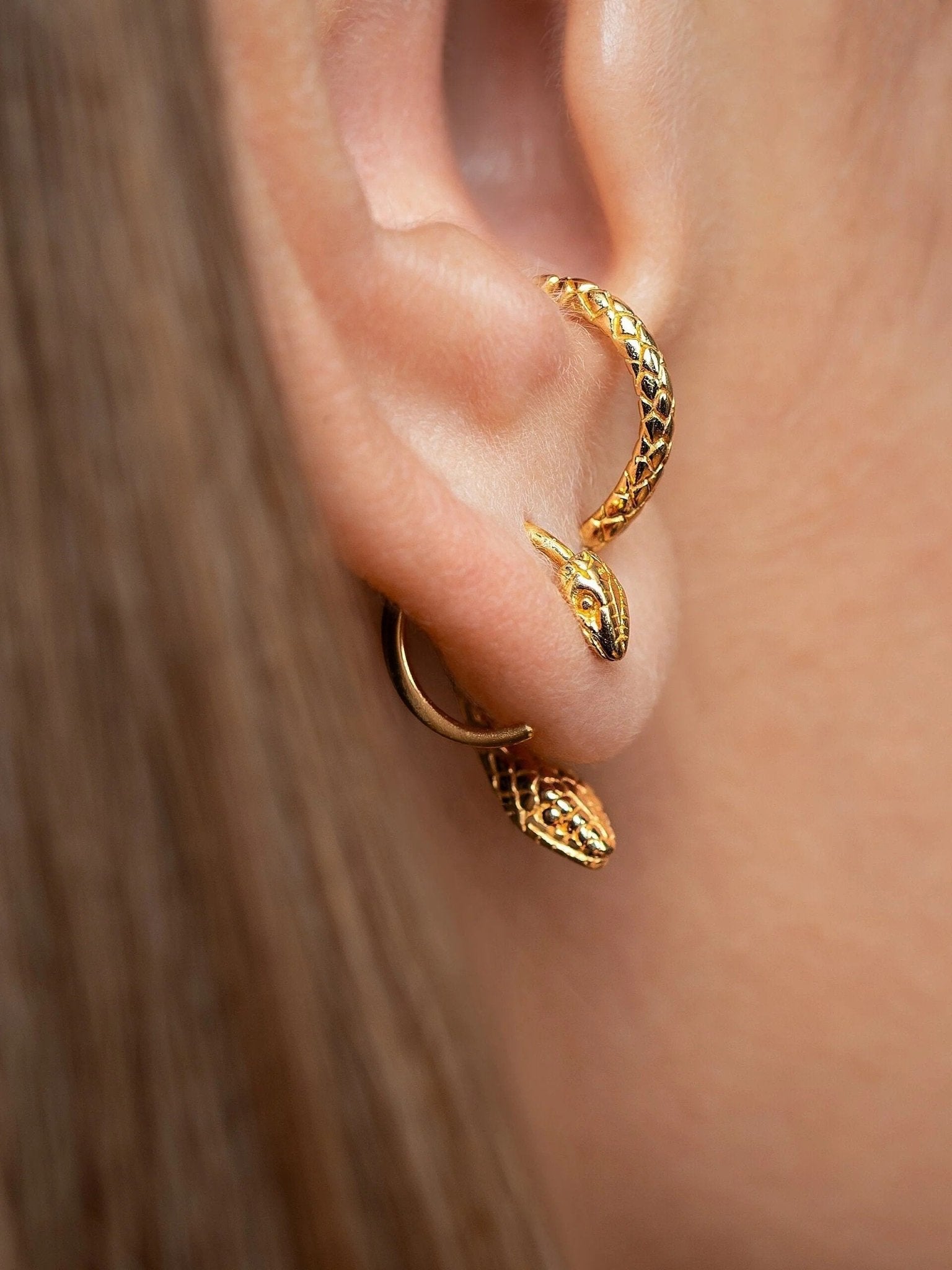 Gold-plated snake hoop earrings on a white background, featuring intricate detailing and a sleek, elegant design.