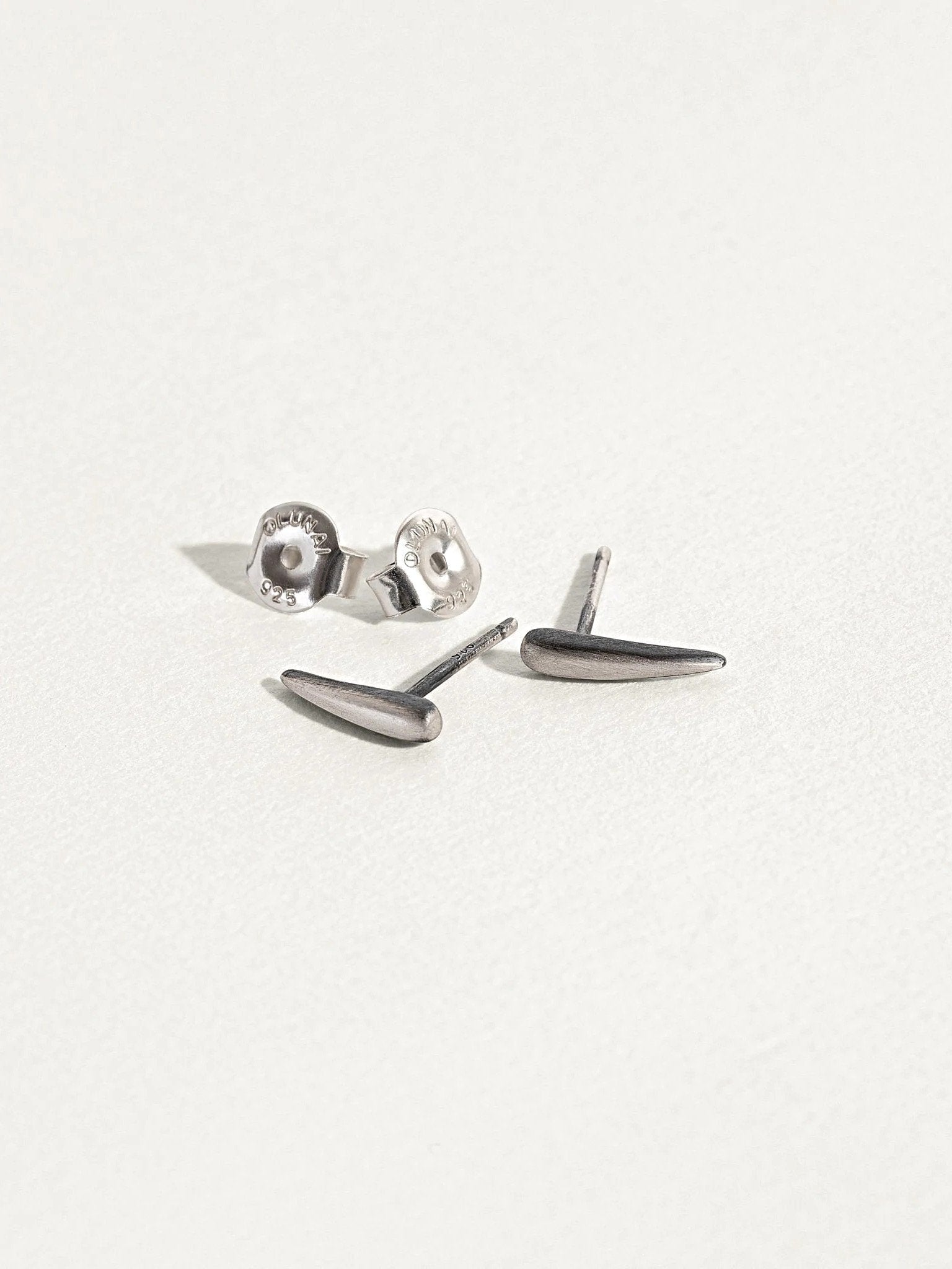 "Aura Dainty Tusk Earrings in silver oxide with screw backs on neutral background"