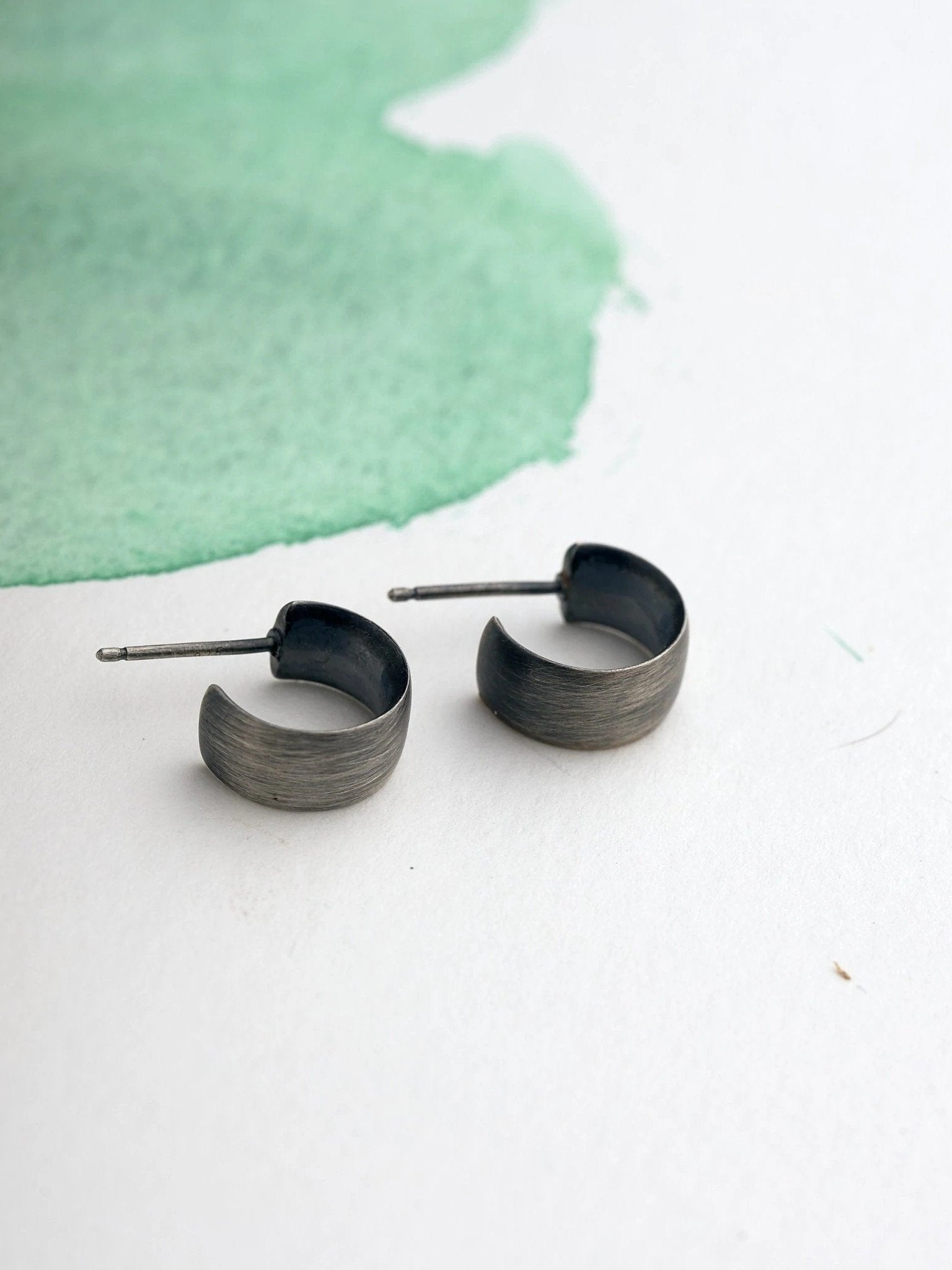 Flat-lay of oxidized silver hoop earrings on watercolor green paper.