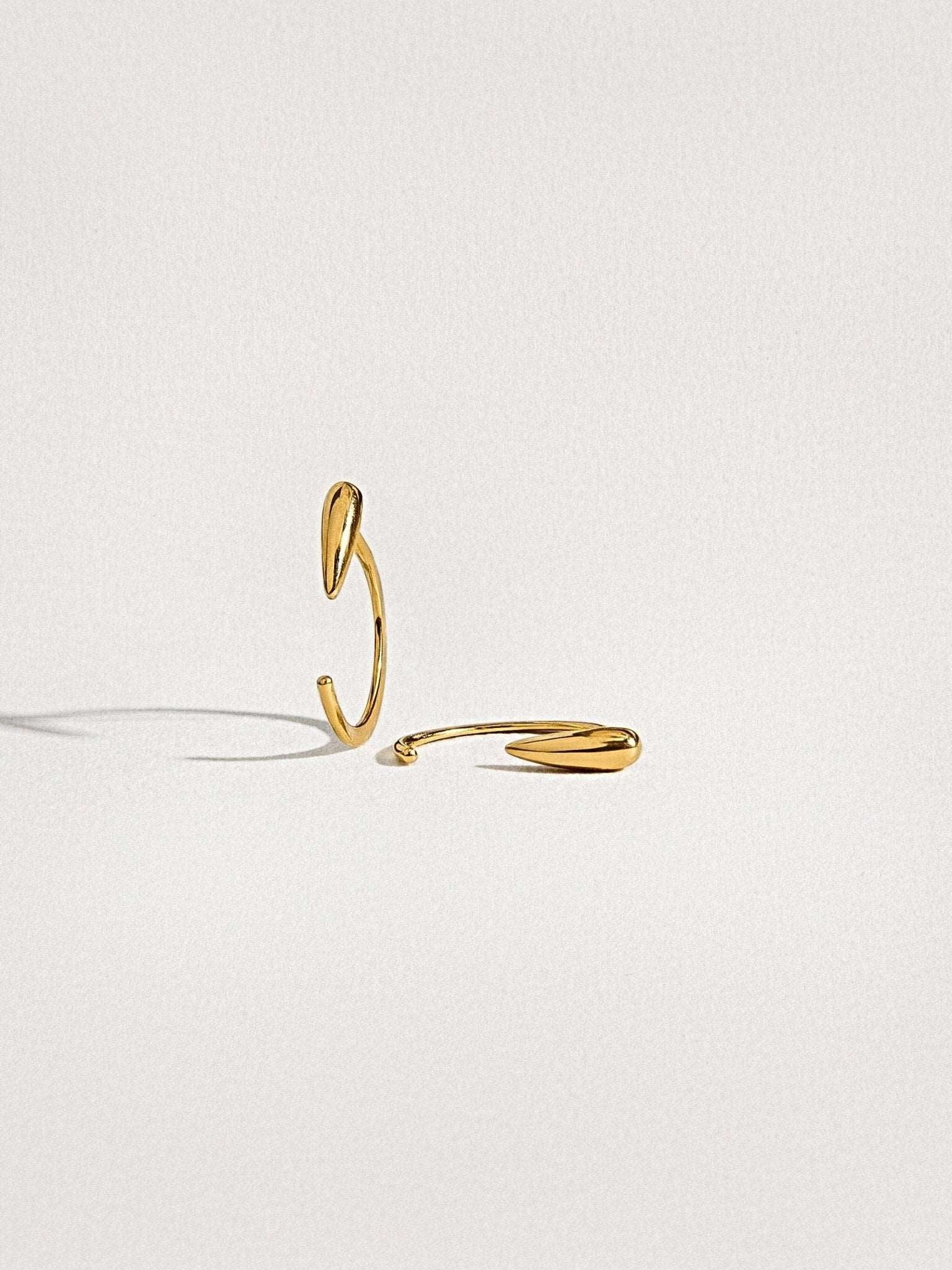 Luppa hug hoop earrings in 24K gold plated finish — sculptural tusk-inspired shape on white background.