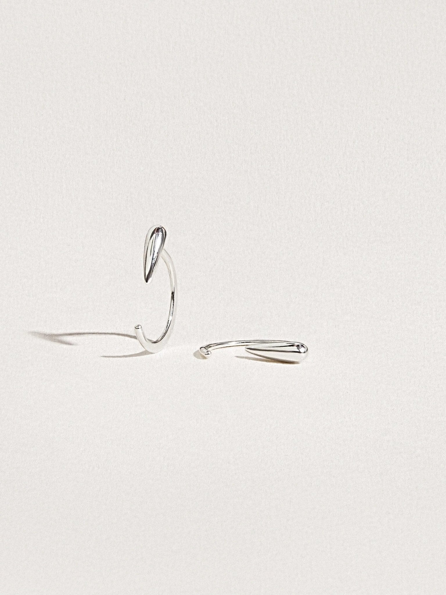 Luppa hug hoop earrings in sterling silver — elegant open curve on soft background.