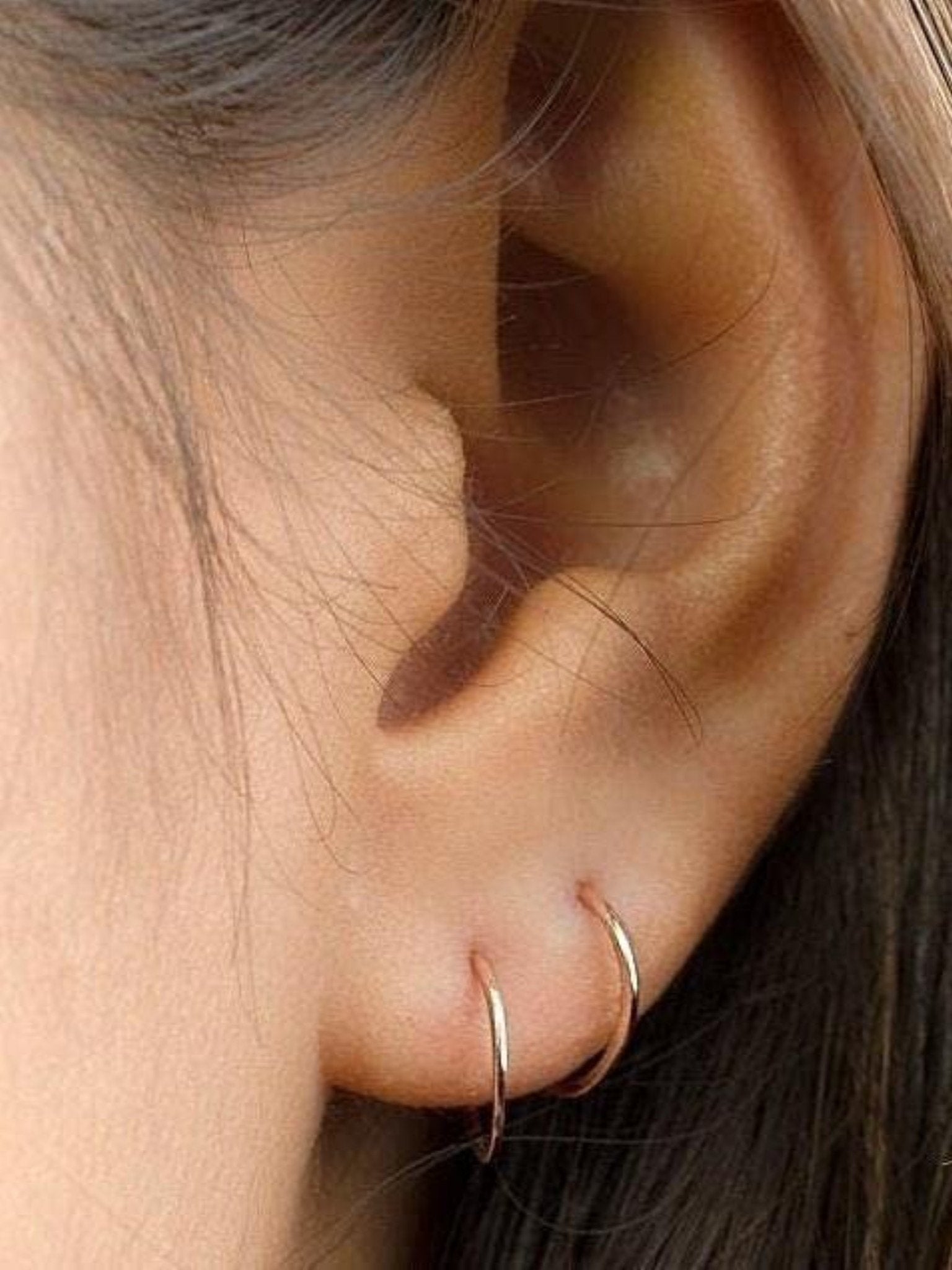 Minimalist gold hoop earrings worn on a model’s ear, side view.