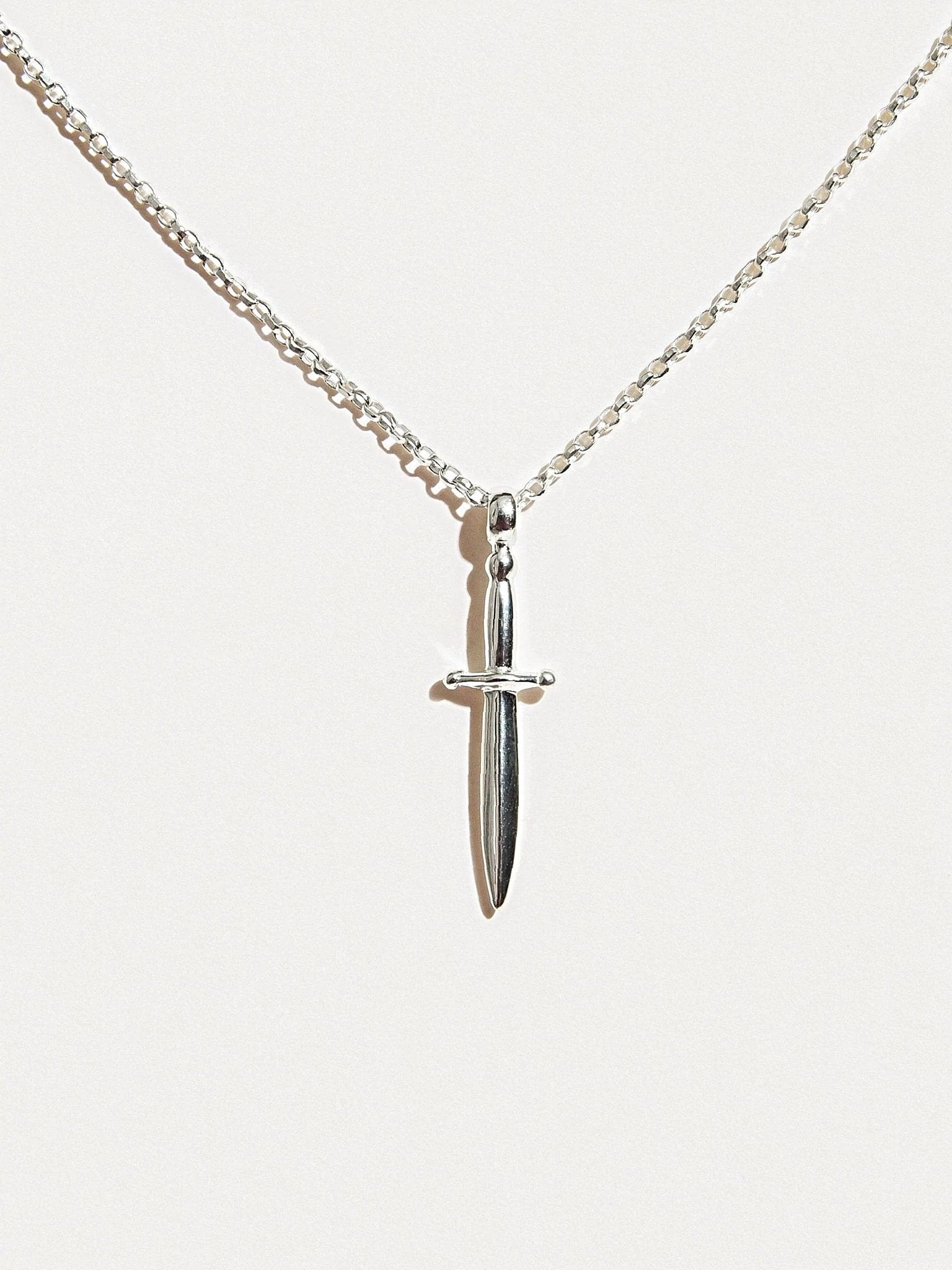 Sterling silver dagger necklace hanging on white background, clean full view.