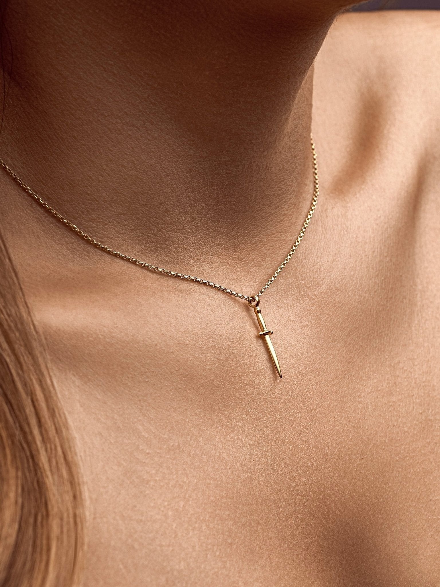 Gold dagger necklace hanging alone on neutral background, minimalist tone
