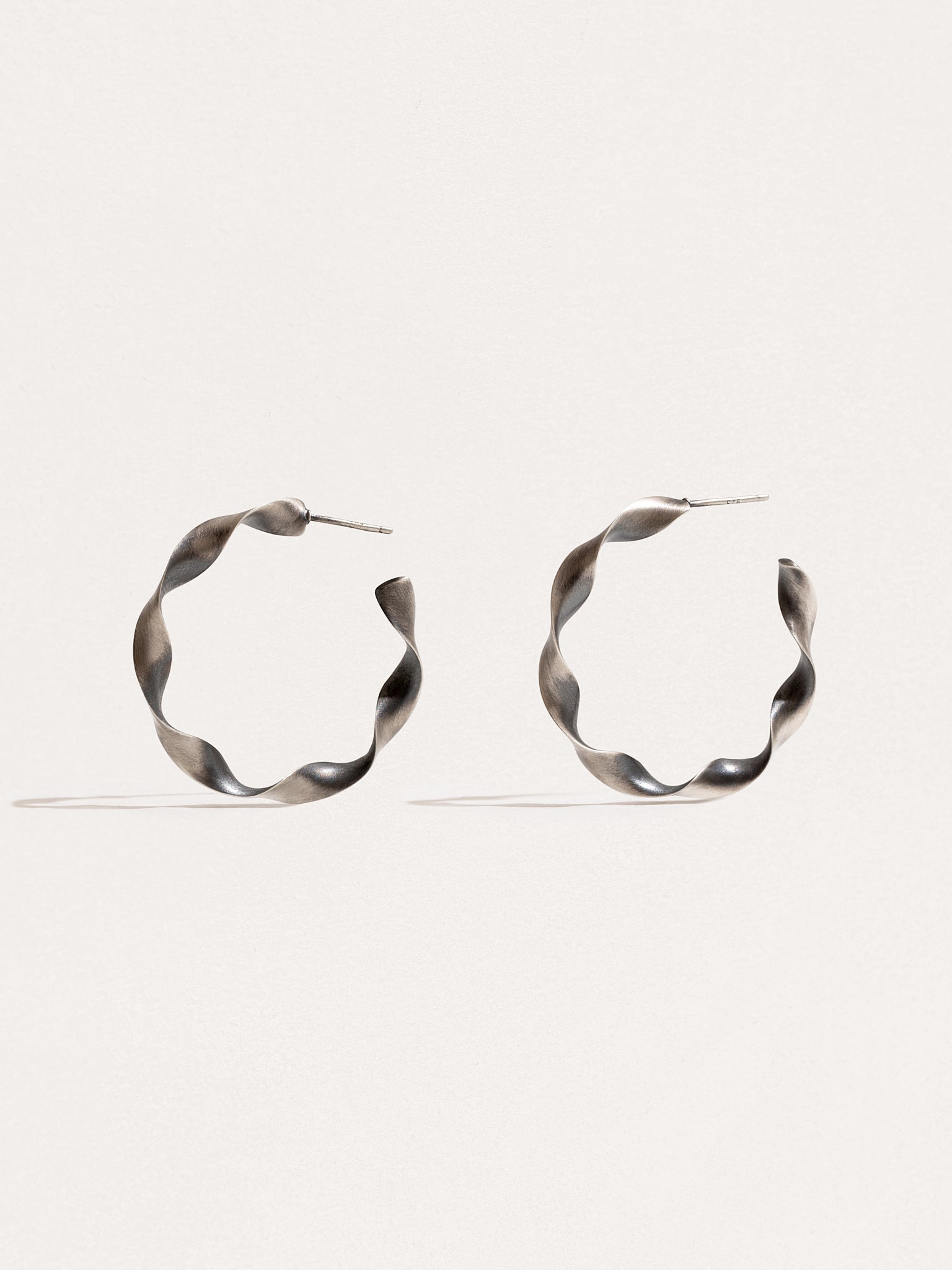 "Gene Twisted Hoop Earrings in silver oxide on neutral background"