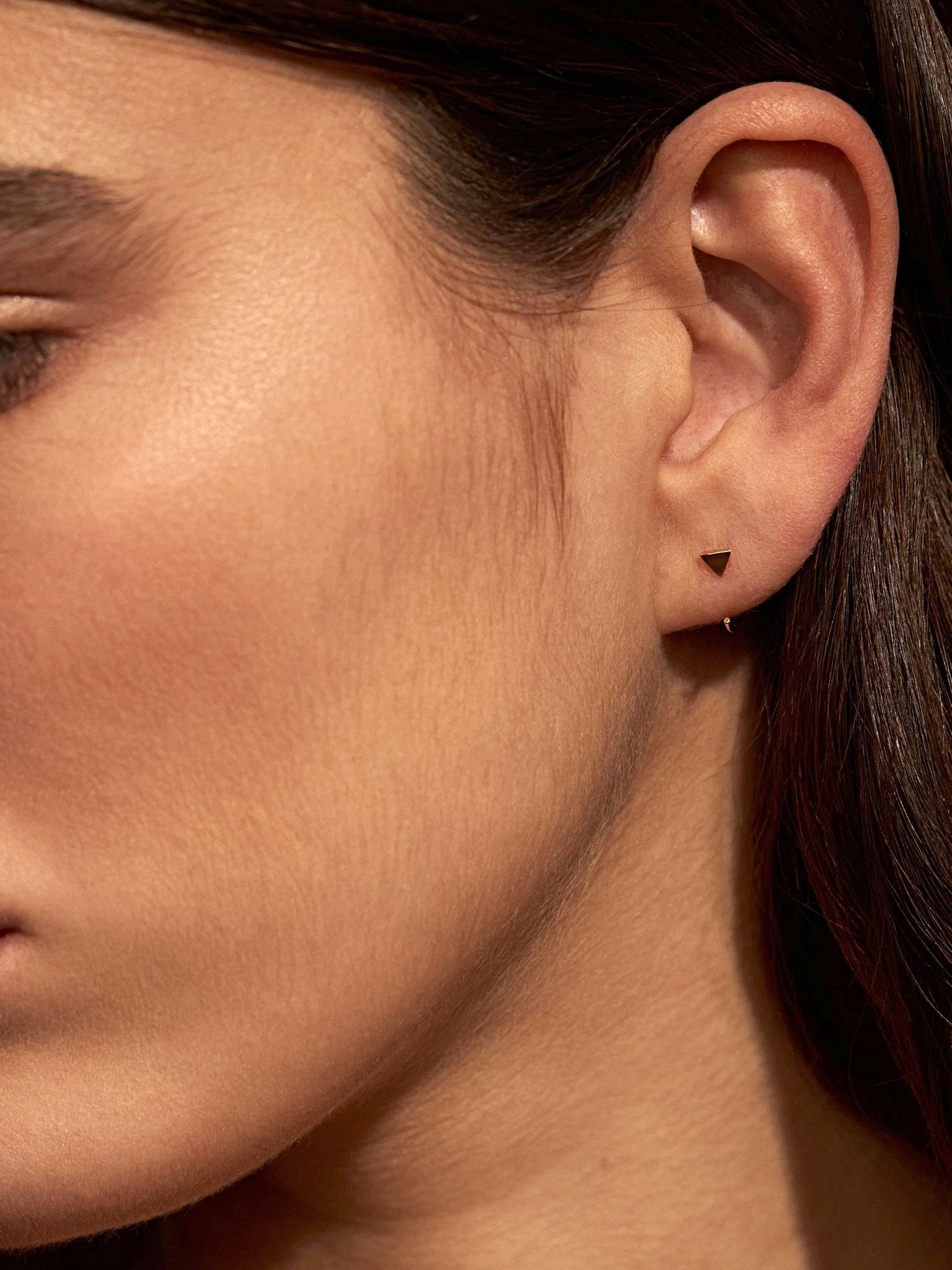 	Close-up of model wearing yellow gold geometric triangle huggie earrings