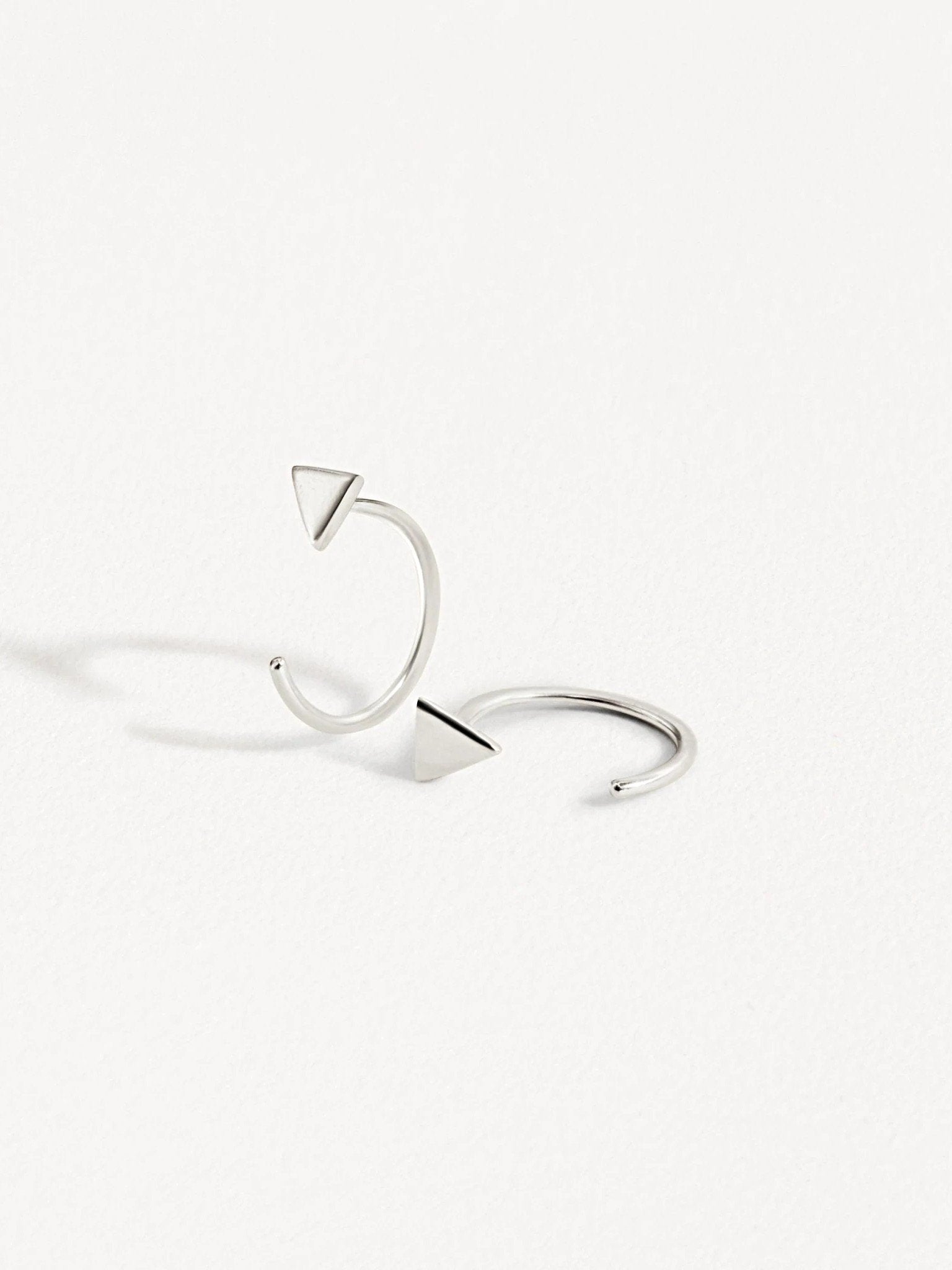Pair of silver geometric triangle huggie earrings on white background