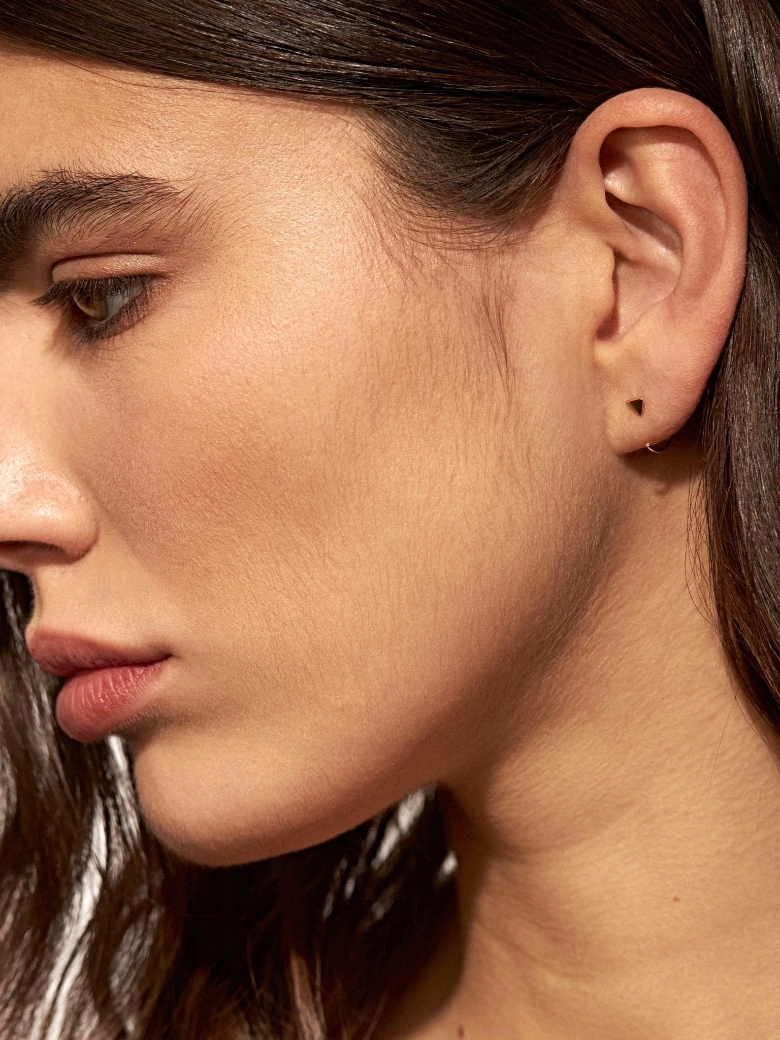 Model wearing geometric triangle huggie earrings in yellow gold